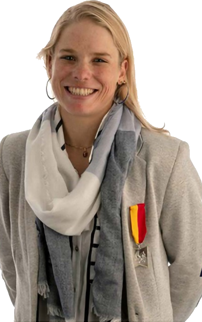 Alexandra Tondeur souriante, veste grise et écharpe, portant la médaille du mérite wallon.