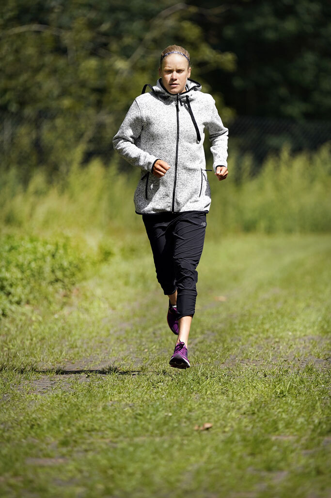Alexandra Tondeur court sur un chemin d'herbe en lisière de forêt, en veste polaire grise.