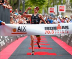 Alexandra Tondeur franchit la ligne d'arrivée de l'IRONMAN 70.3 France, bras levé.